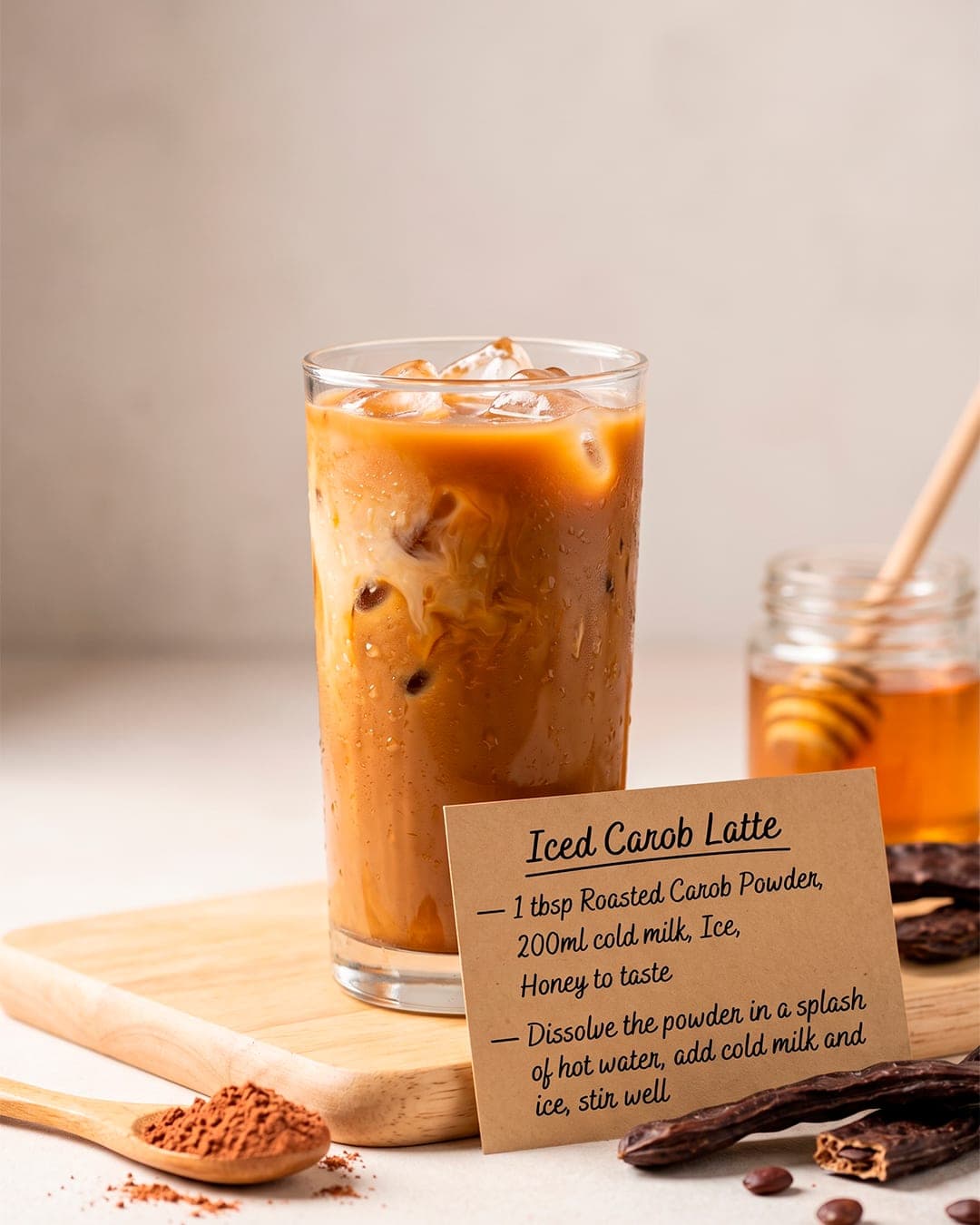 Iced carob latte on a wooden board with a jar of honey and whole carob pods